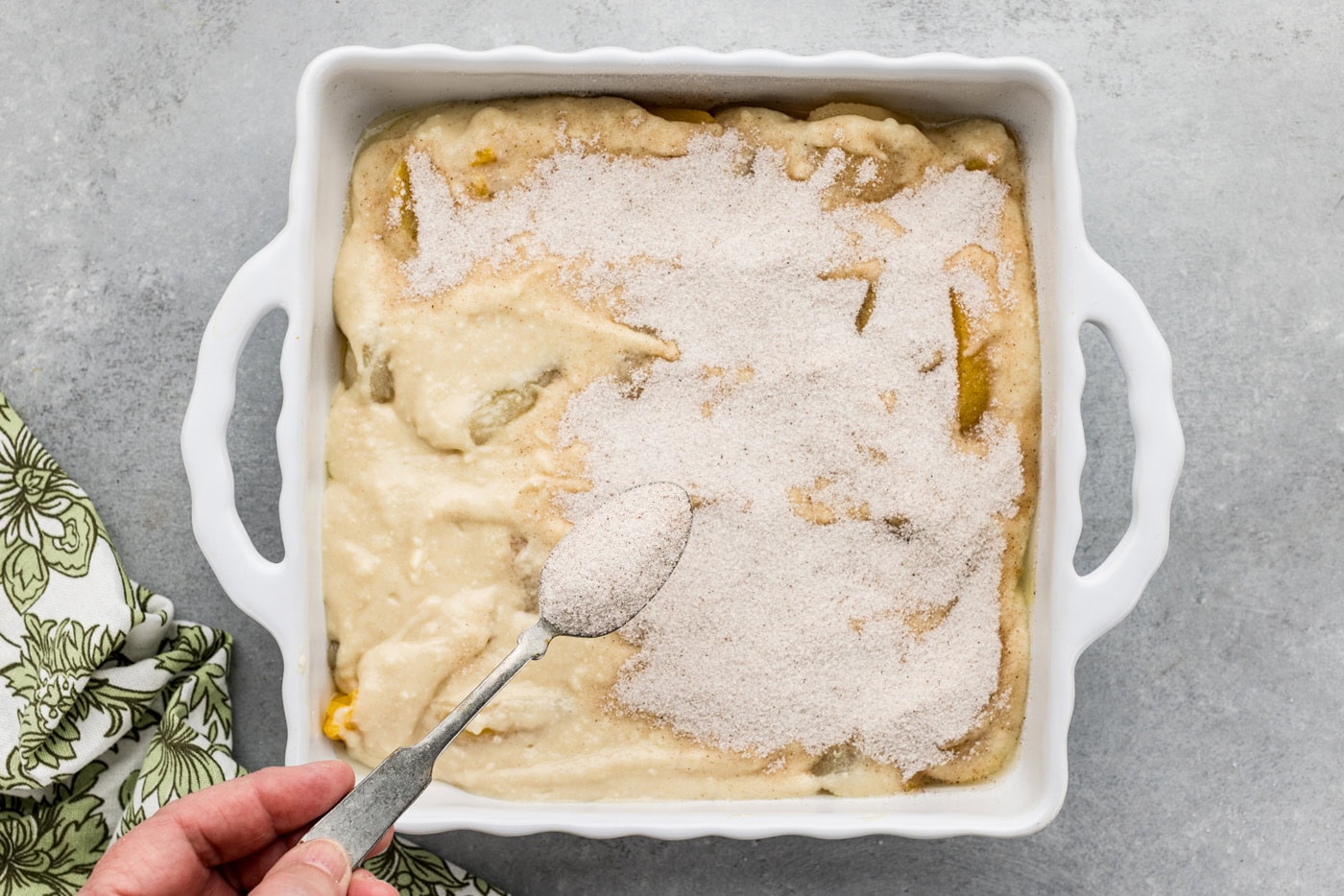 spoon sprinkling on sugar mixture over cobble batter in a dish