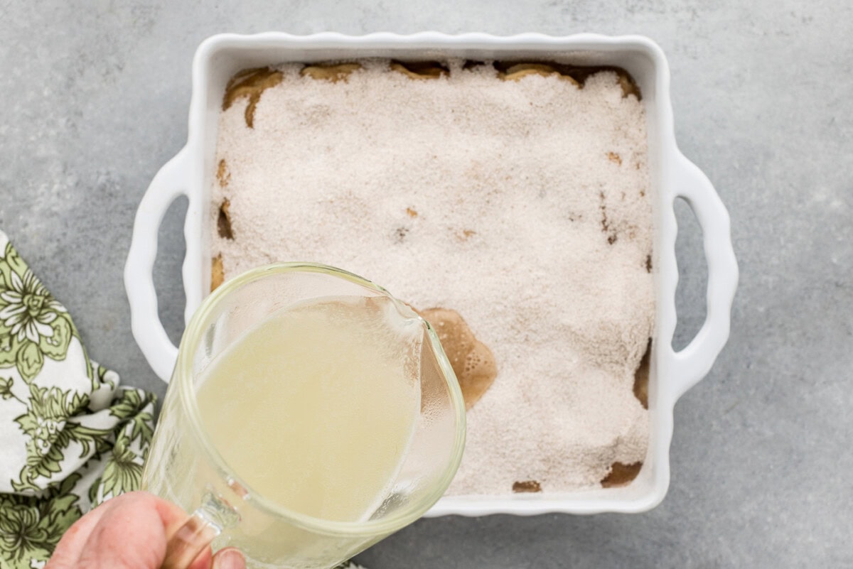 pouring warmed fruit juices over unbaked cobbler in a baking dish