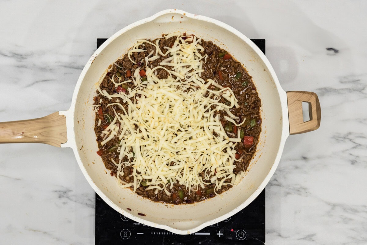 shredded provolone cheese on top of philly cheesesteak sloppy jooe mixture in a skillet