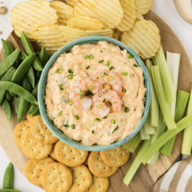 Close up photo of a bowl of Shrimp Dip surrounded by chips and veggies