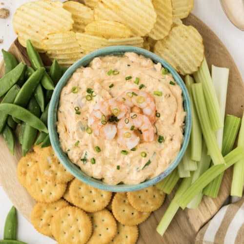 Close up photo of a bowl of Shrimp Dip surrounded by chips and veggies