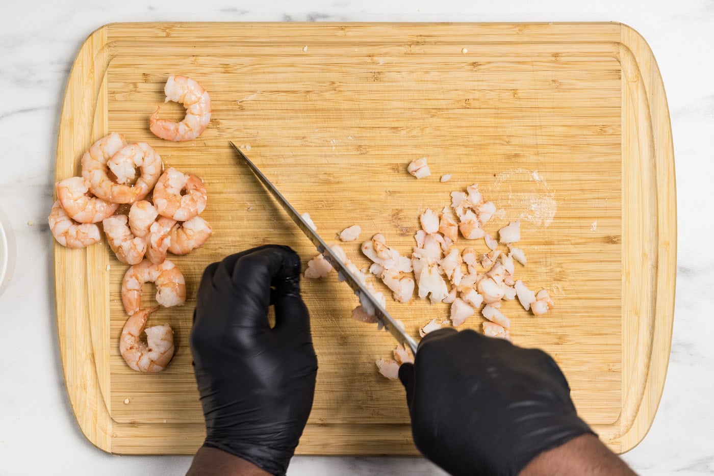 Hands using a knife to chop up shrimp on a cutting board