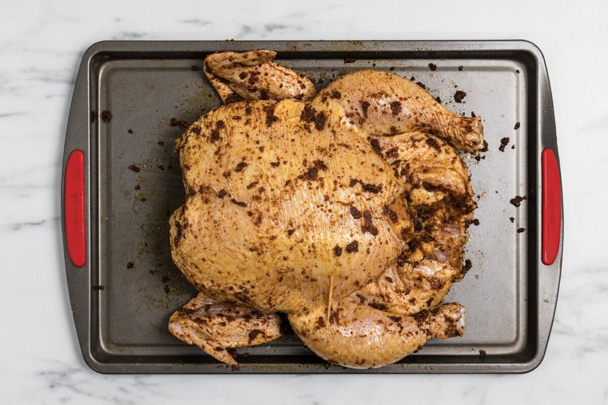 whole raw chicken coated in oil and spice rub on a baking sheet