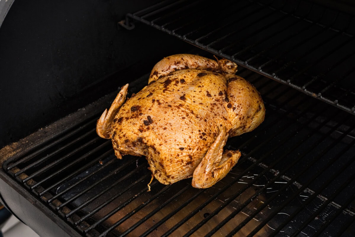 seasoned whole chicken on smoker grates