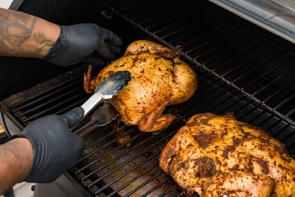tongs flipping whole chicken upside down on a smoker grate