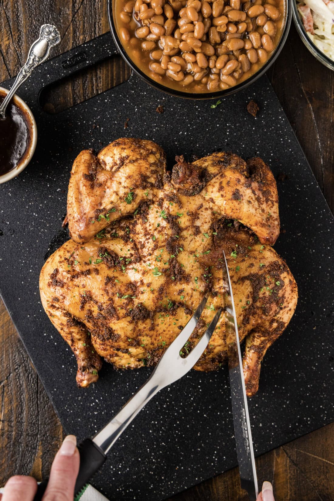 Smoked Spatchcock Chicken on a black board being carved with a fork and knife