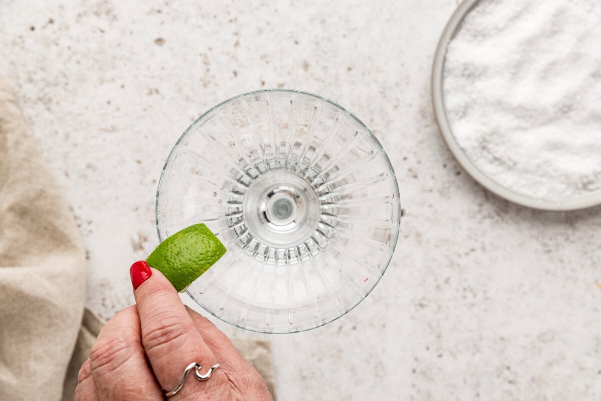 hand rubbing a lime wedge over the rim of a margarita glass