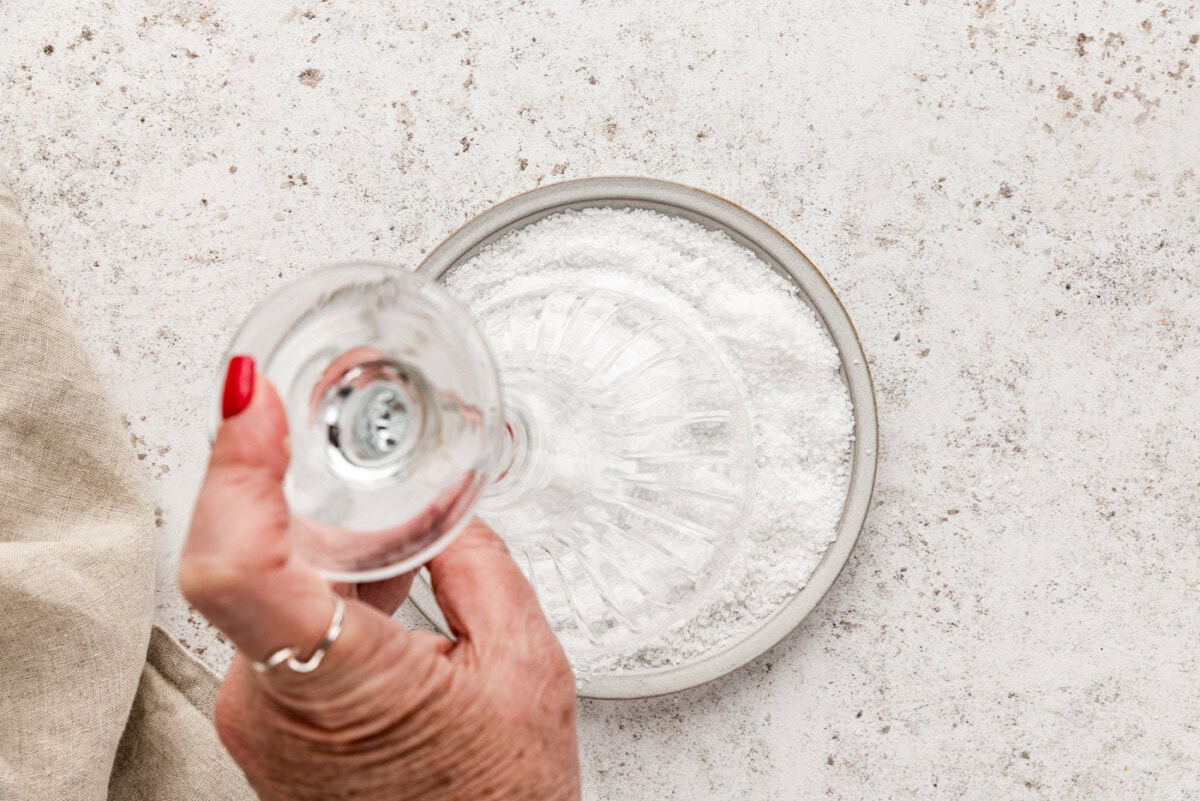 hand holding a martini glass upside down and dipping it in rimming salt