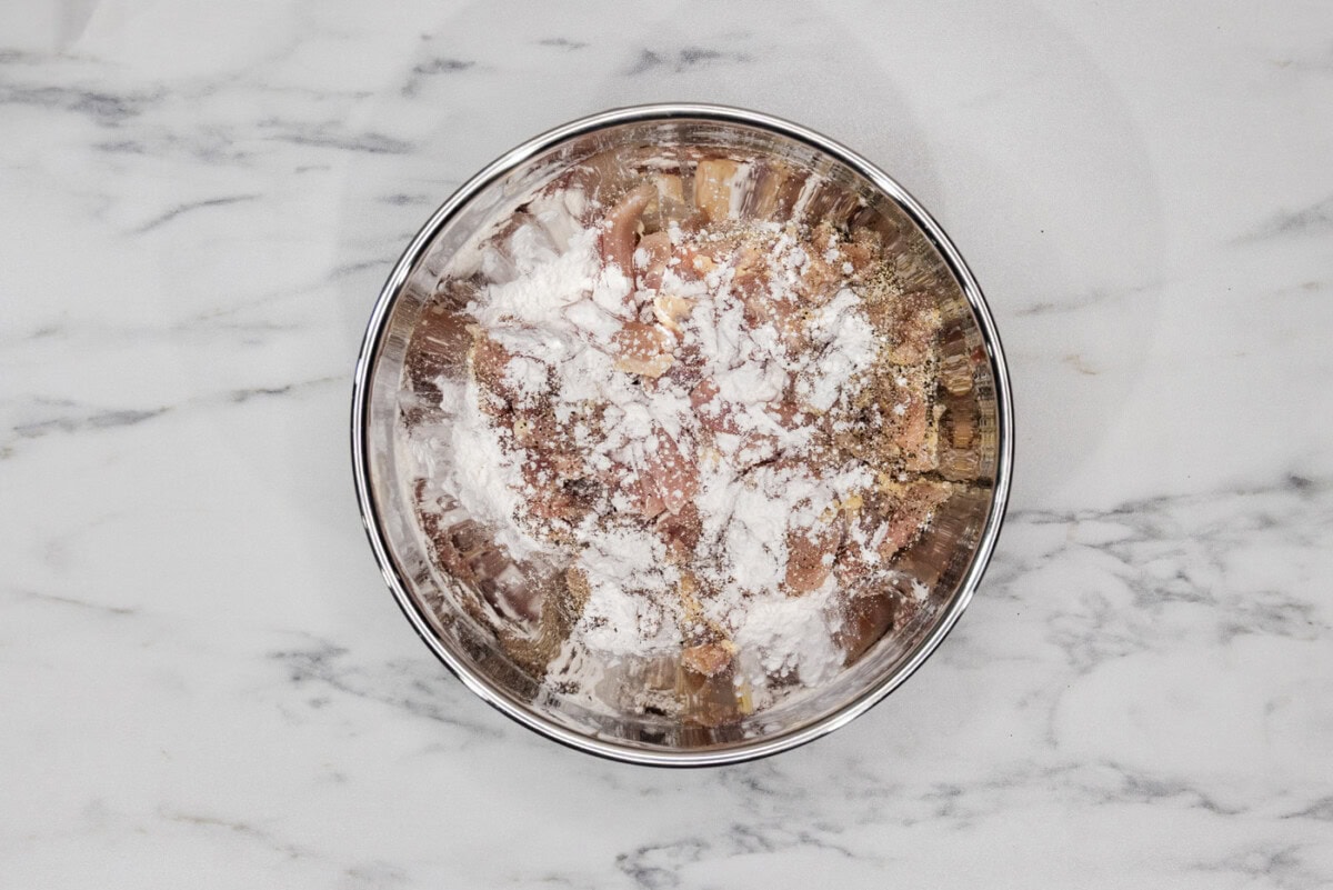 sliced chicken in a bowl with cornstarch sprinkled on top