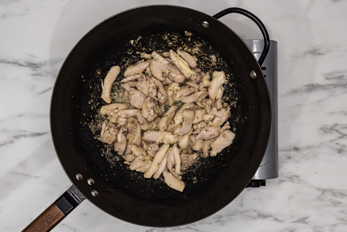 cooked sliced chicken in a wok with oil