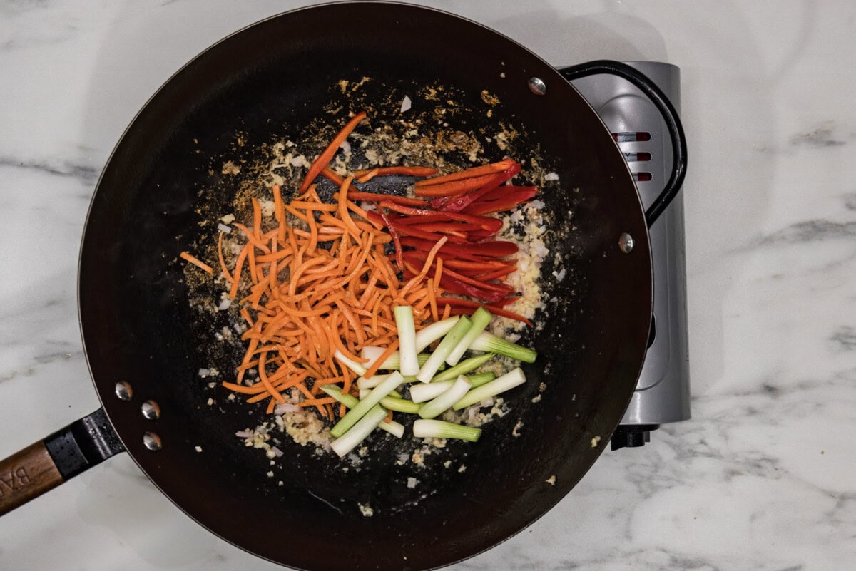 julienned red pepper, green onions, and carrots in a wok with oil