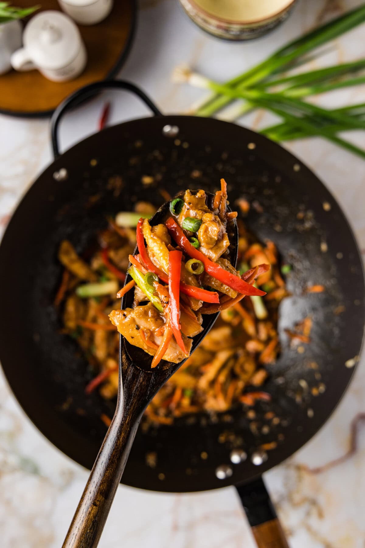 Spoonful of Szechuan Chicken held above a wok of Szechuan Chicken