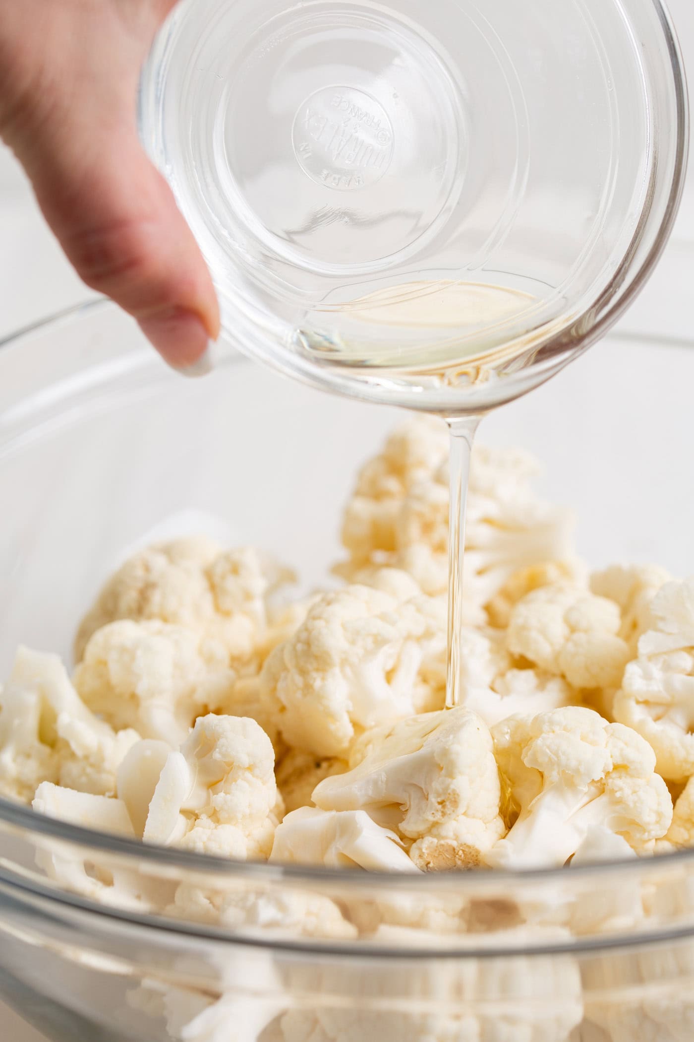 Oil being drizzled over cauliflower in a bowl