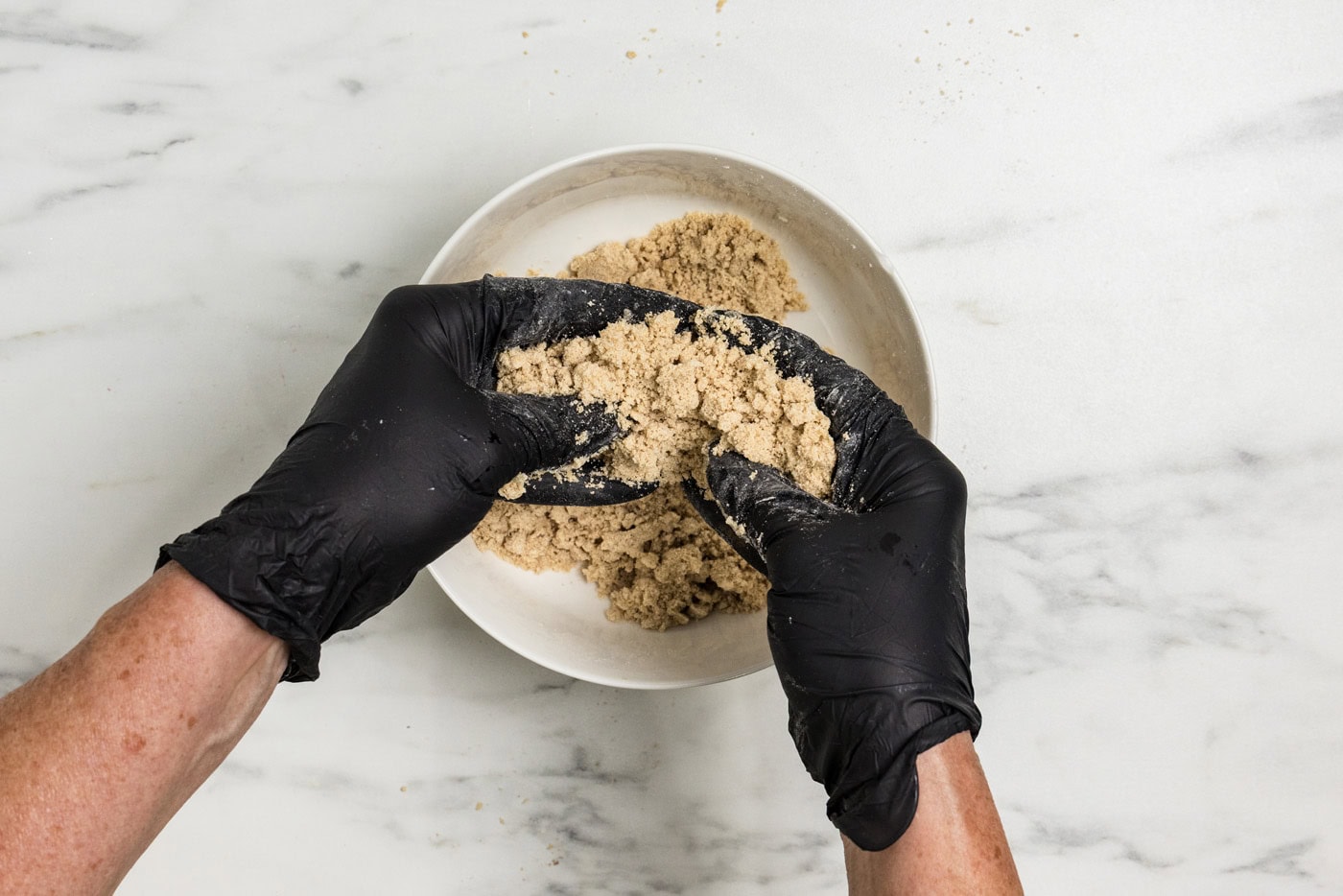 gloved hands squeezing streusel ingredients together in a bowl