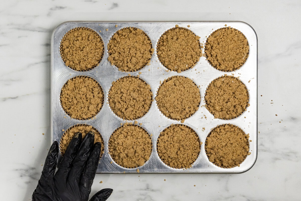 hand pressing down on streusel topping on top of muffin batter