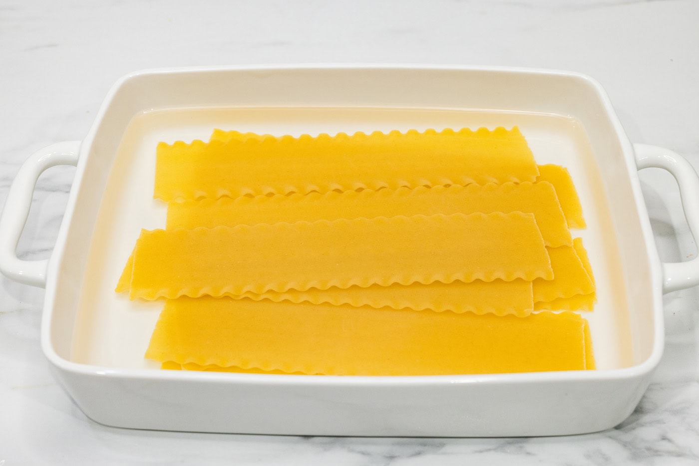 lasagna noodles soaking in water in a baking dish