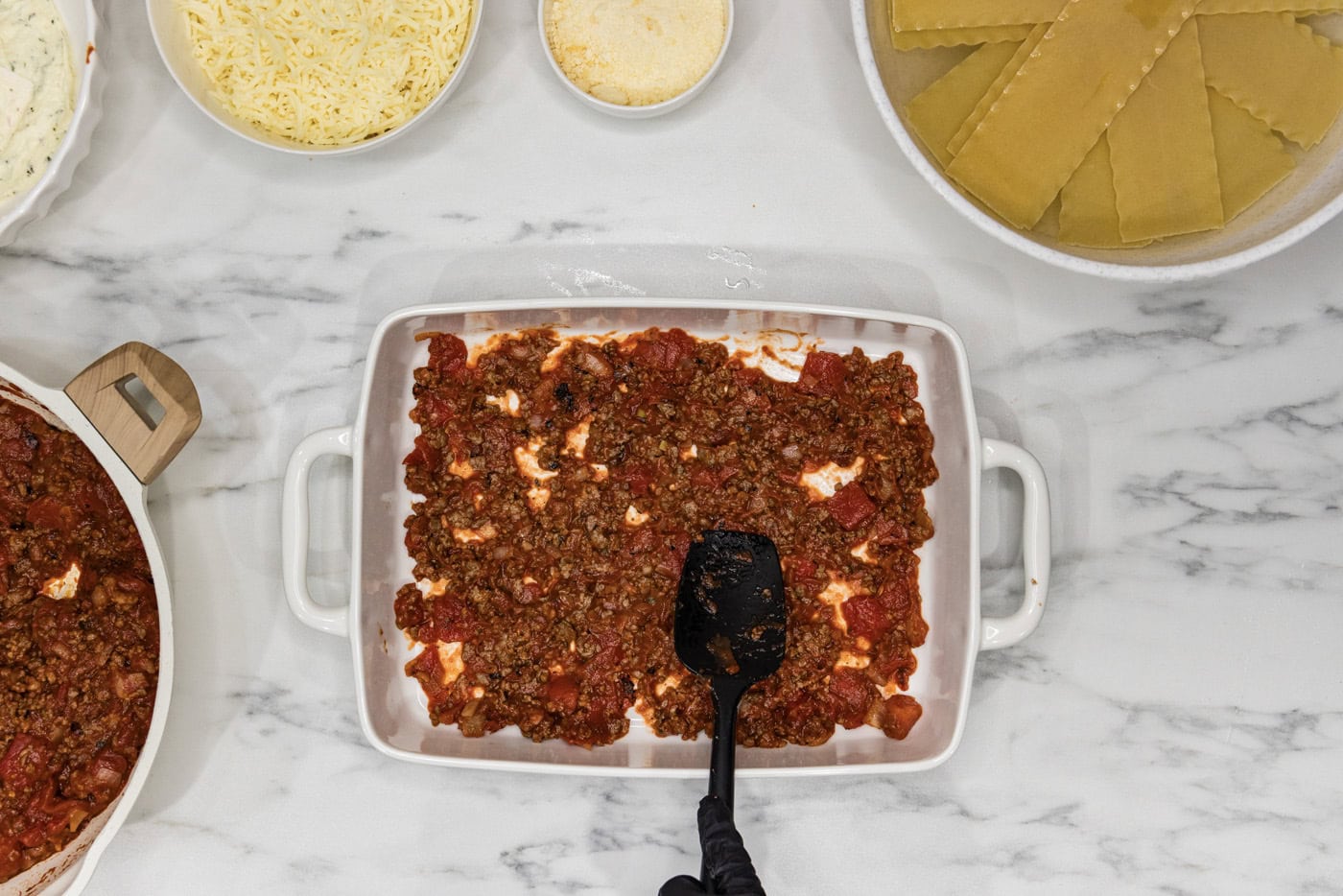 spoon spreading meat sauce mixture on bottom of baking dish