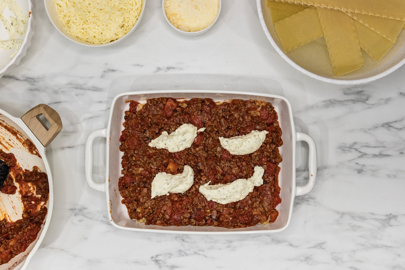 dollops of ricotta cheese on top of layer of meat sauce in a baking dish