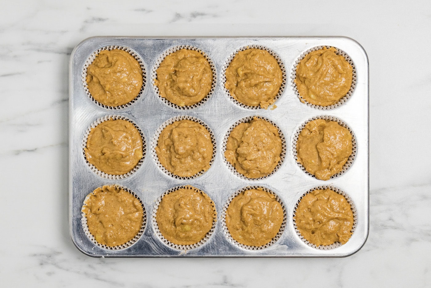 pumpkin banana muffins batter in paper cups inside a muffin pan