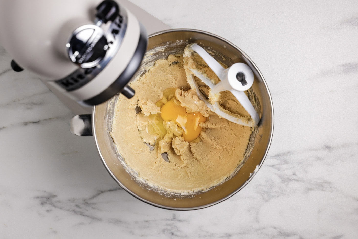 adding eggs to sugar and butter mixture in a stand mixer bowl