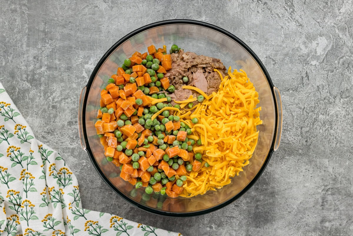 frozen peas and carrots with shredded cheese and tuna in a bowl