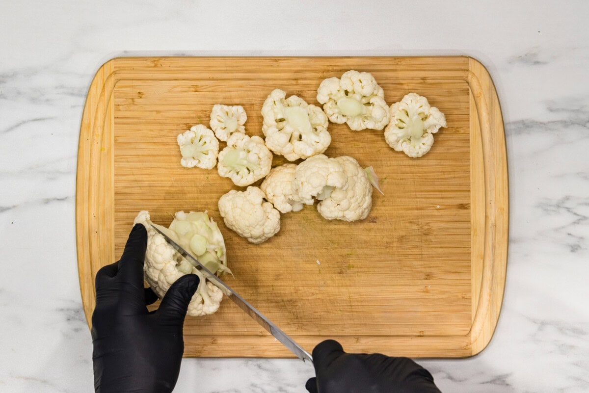 Hand using a knife on a cutting board to cut cauliflower head into florets