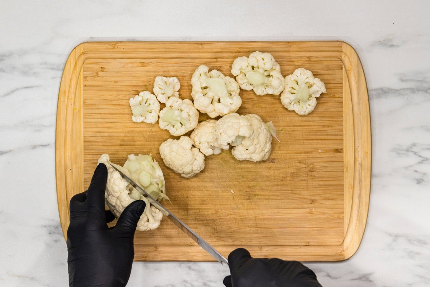 Hand using a knife on a cutting board to cut cauliflower head into florets