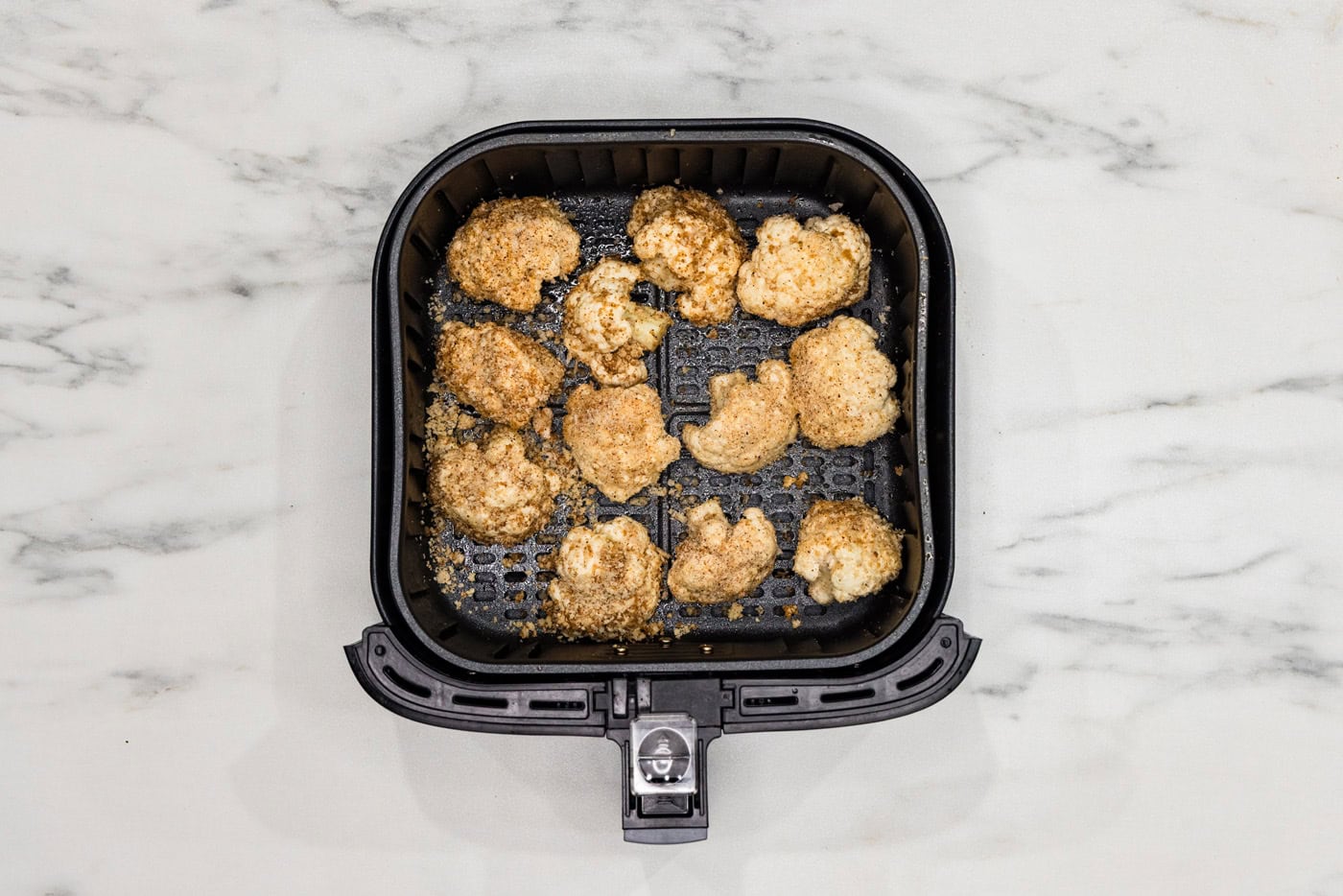 panko coated cauliflower florets in an air fryer basket