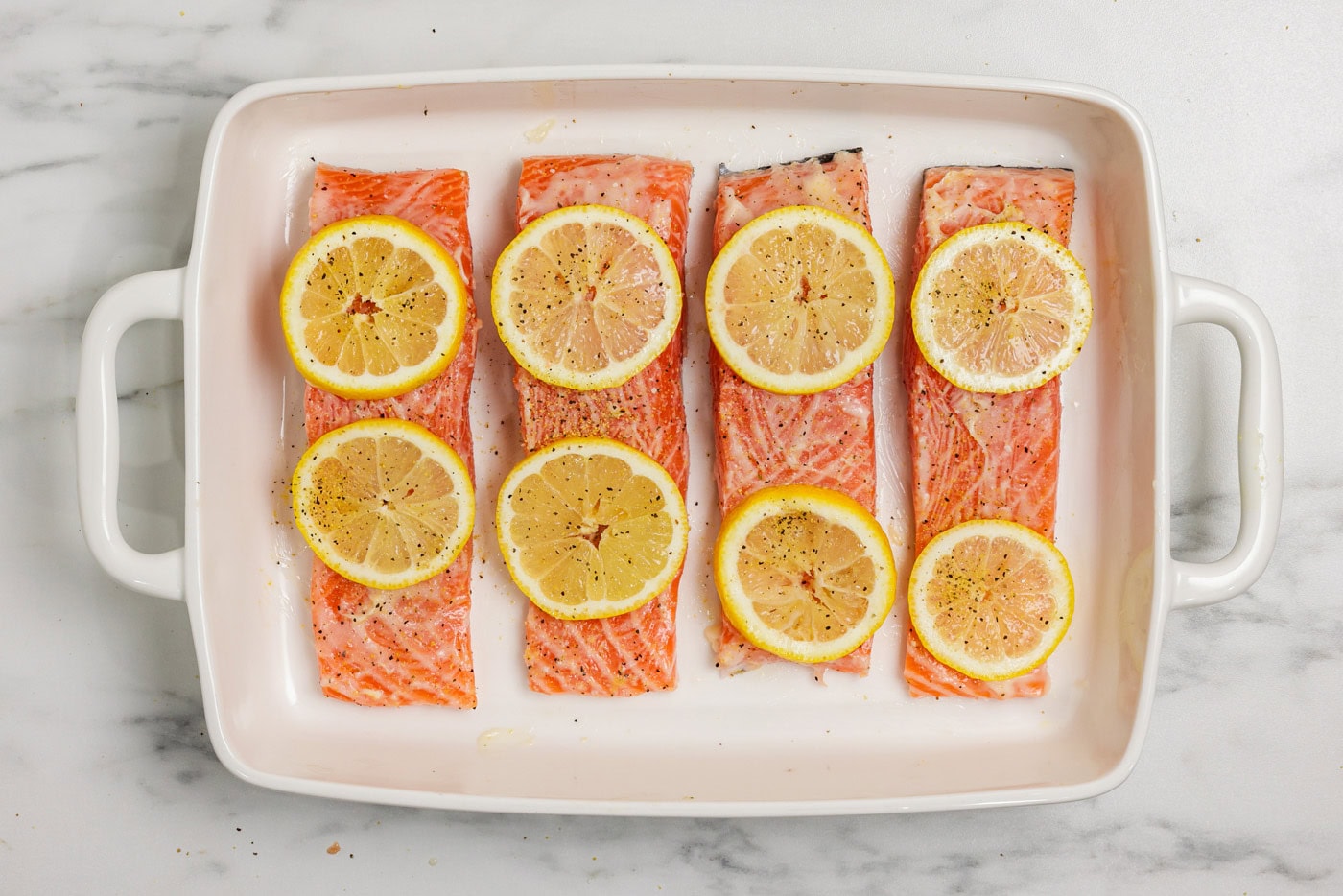 salmon filets topped with lemon butter and sliced lemons in a baking dish