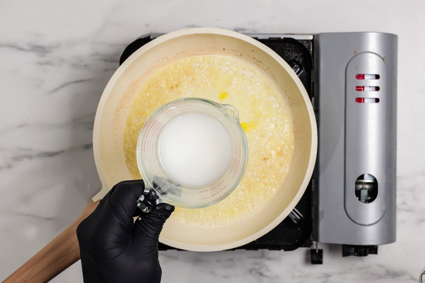 hand holding measuring cup of cornstarch slurry over a skillet of lemon butter sauce