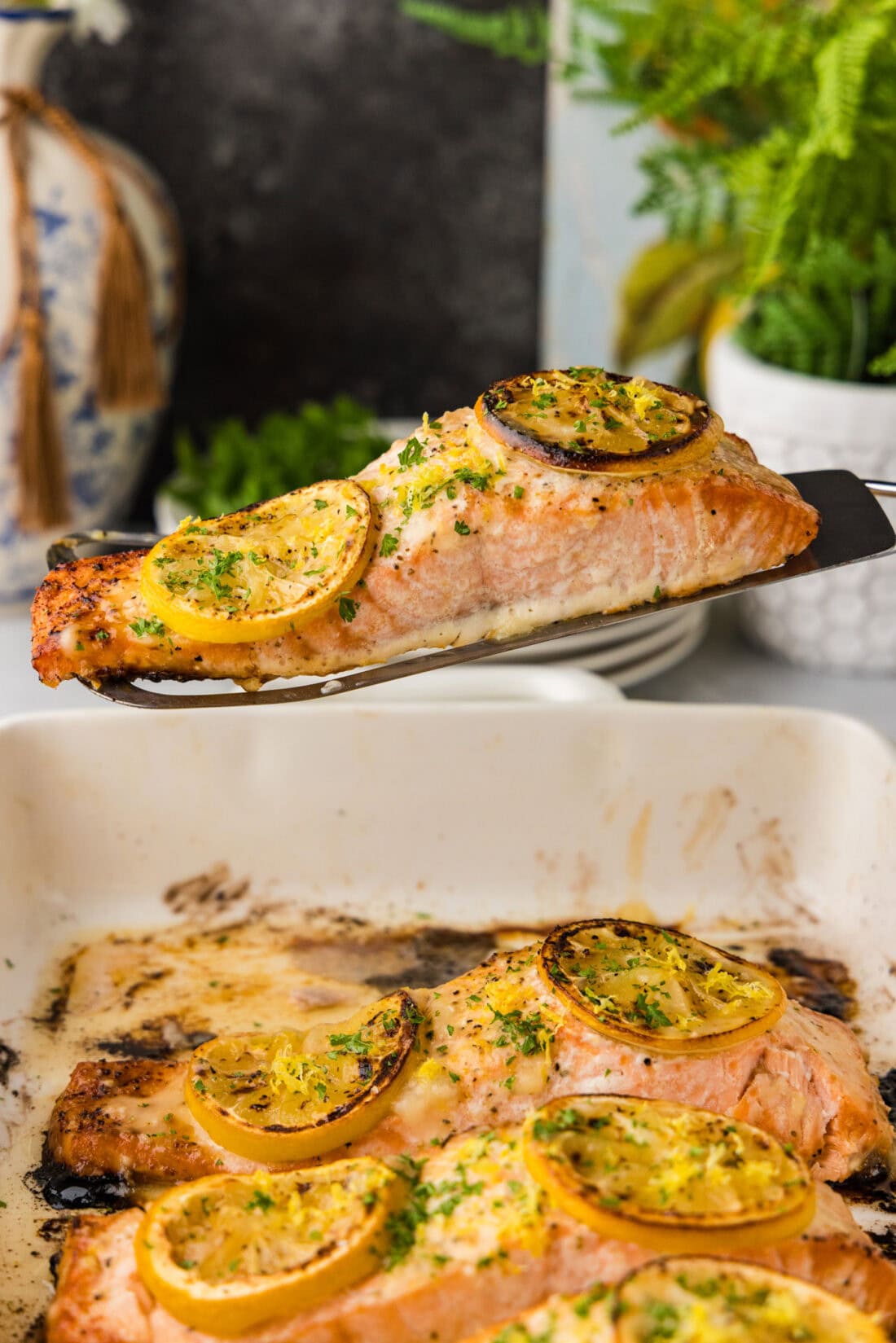 Filet of Baked Lemon Salmon held above a baking dish of more salmon