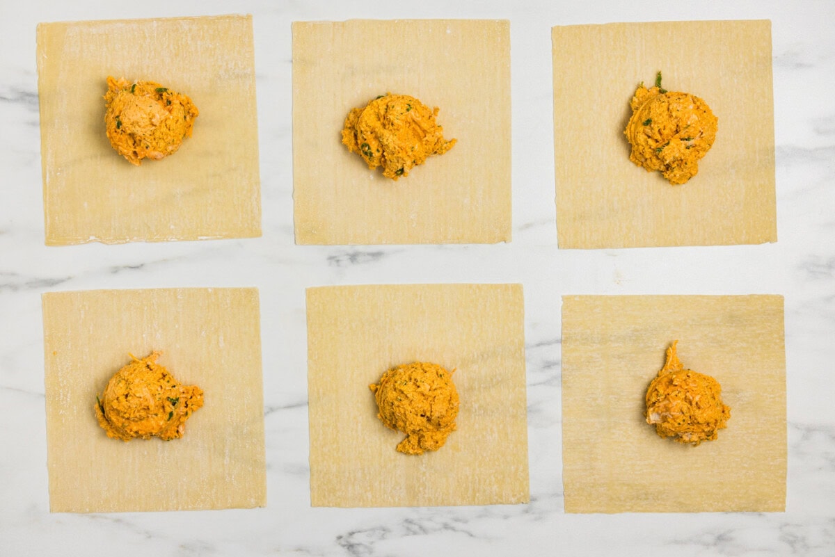 egg roll wrappers on a flat surface with buffalo chicken mixture on top
