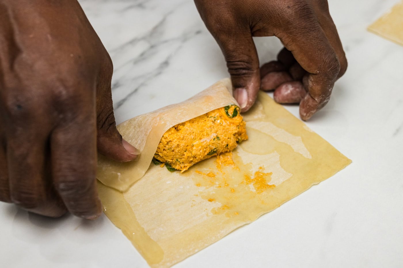 hands folding buffalo chicken mixture into egg rolls