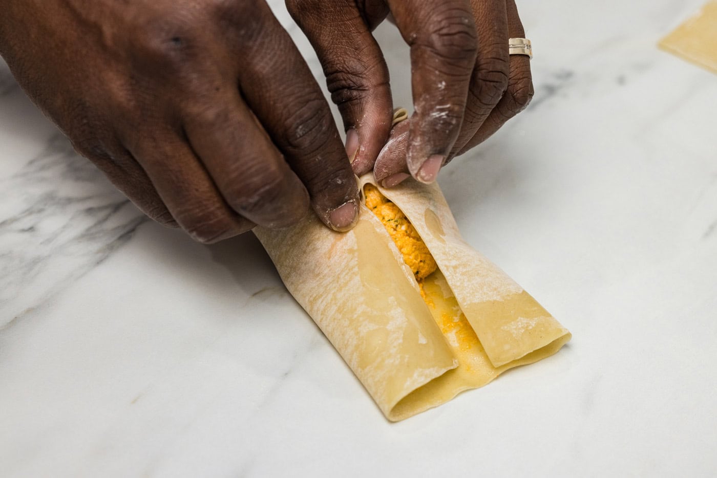 hands rolling egg roll wrapper over filling