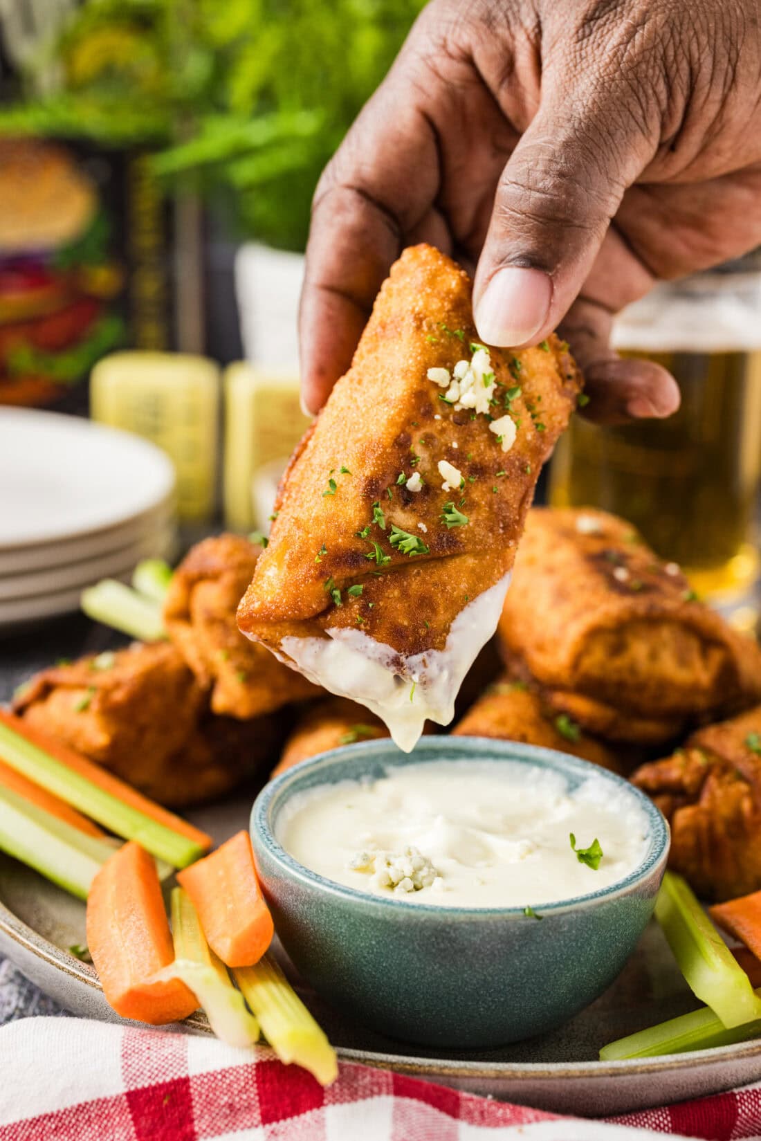 Hand holding a Buffalo Chicken Egg Roll dipped in blue cheese dressing