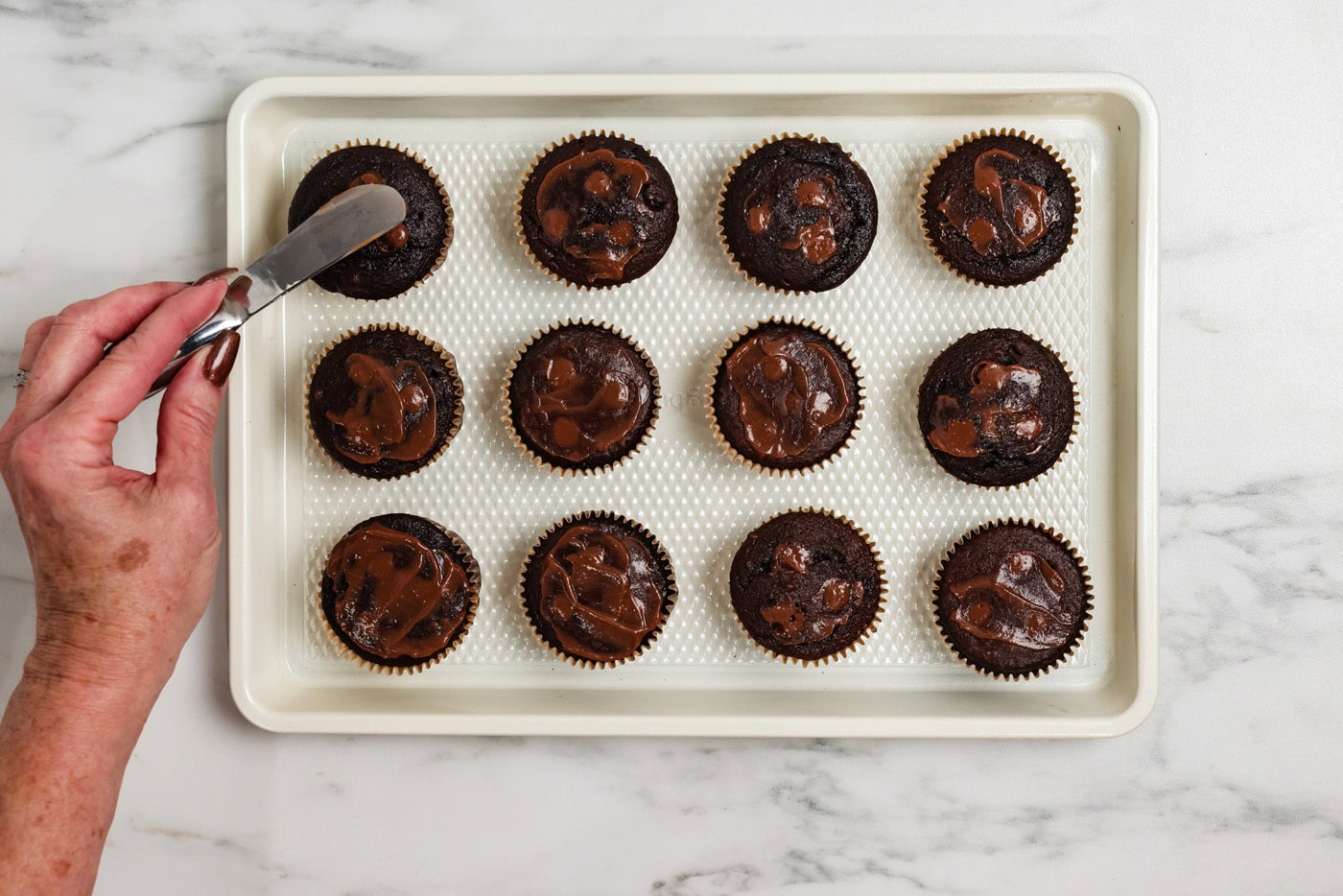 using a small spatula to smear chocolate pudding over the cupcake holes