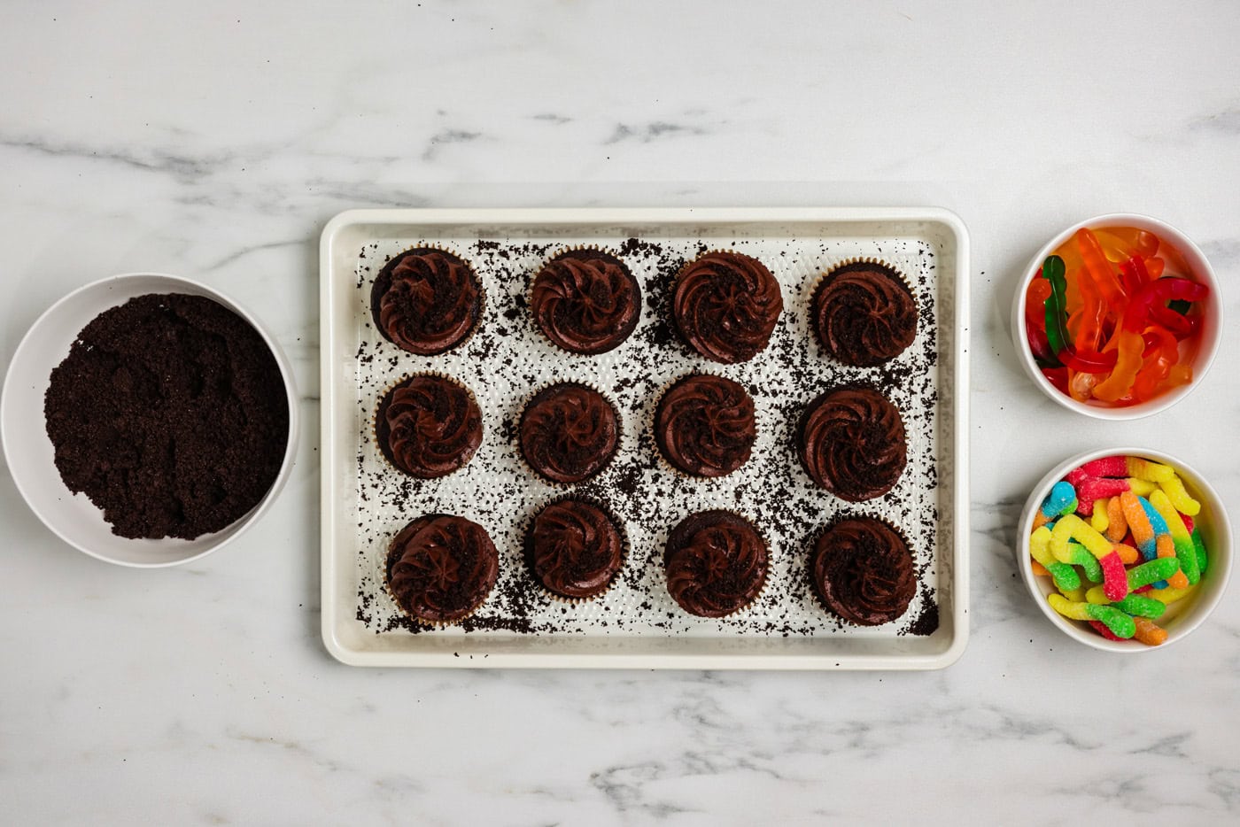 Crushed Oreos sprinkled over chocolate frosted cupcakes on a baking sheet