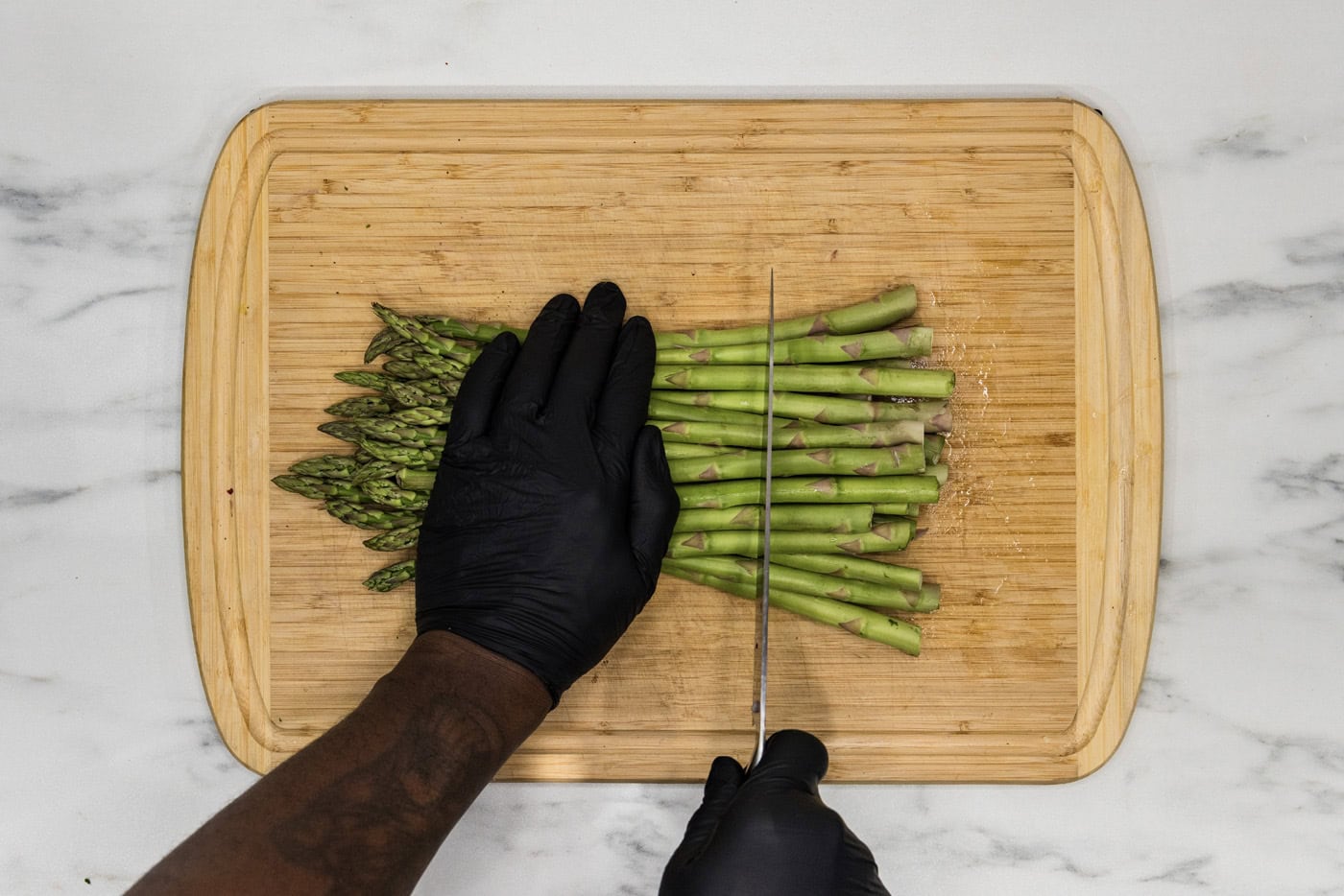 Cutting the woody ends of the asparagus off using a knife on a cutting board