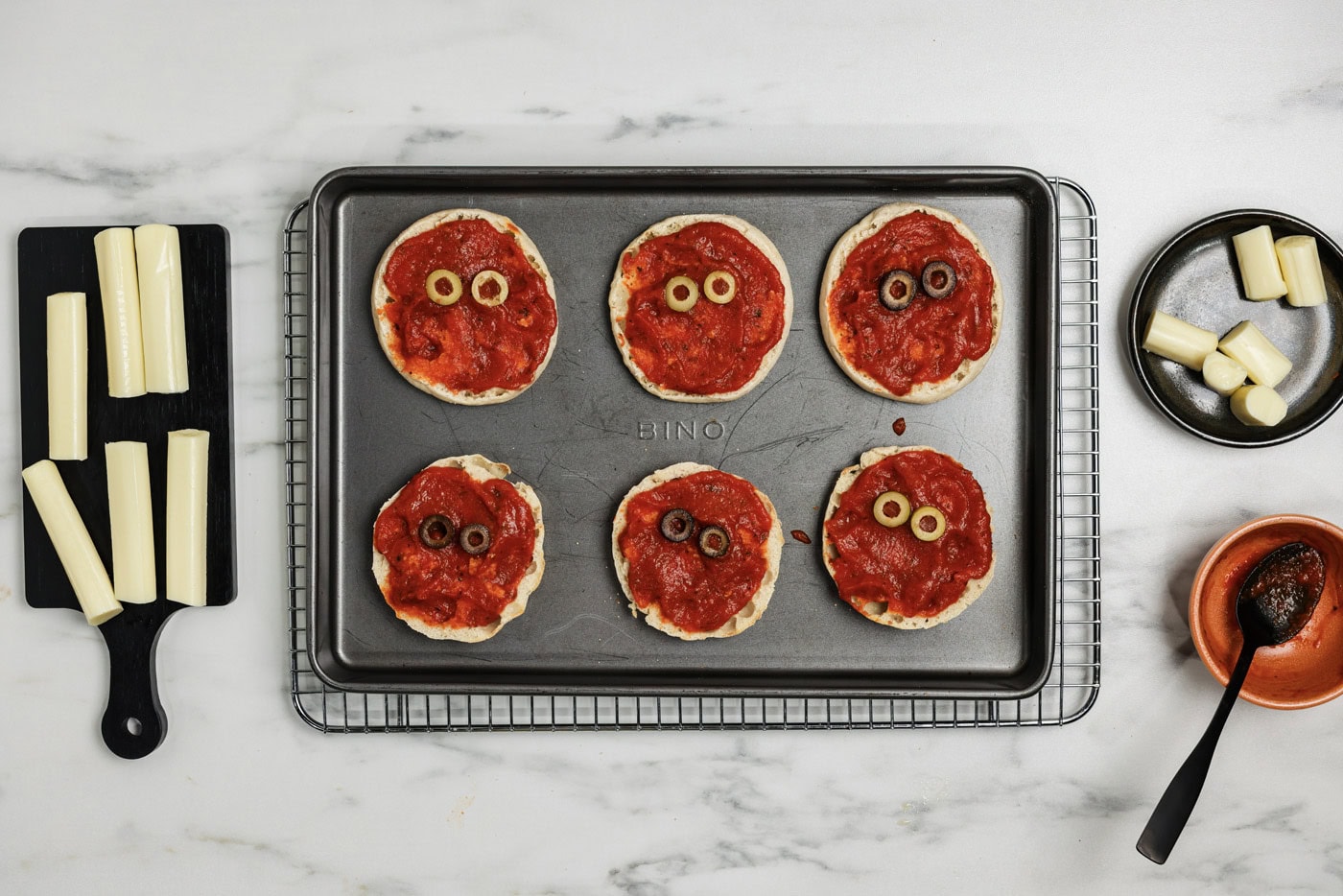 Sliced olives placed on top of sauced English muffins to look like eyes