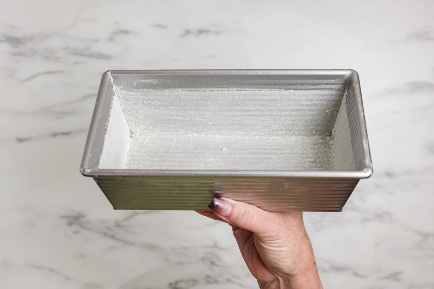 hand holding a greased and flour loaf pan