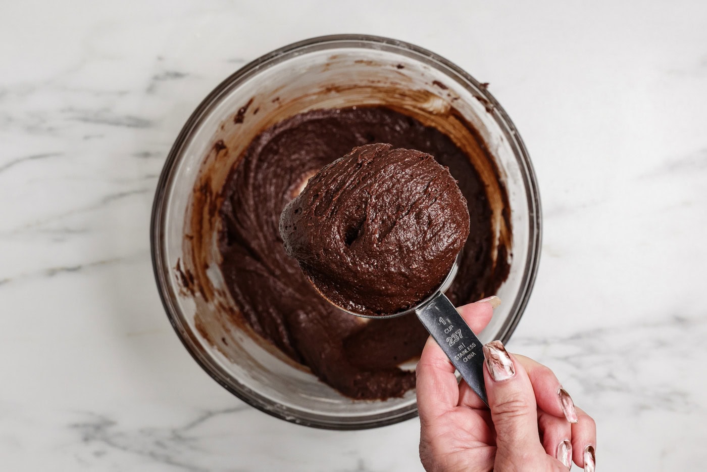 Scooping 1 heaping cup of brownie batter with a measuring cup