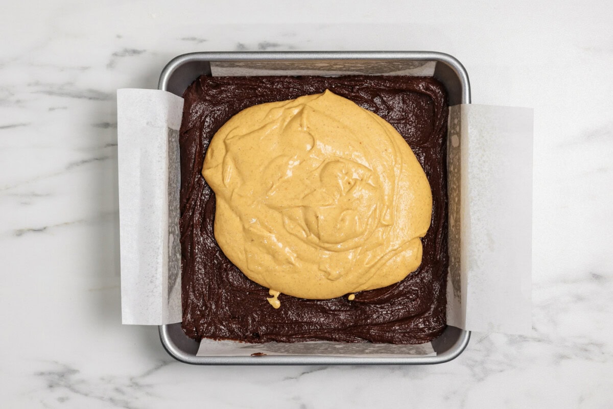 pumpkin cheesecake batter on top of brownie batter in a baking pan