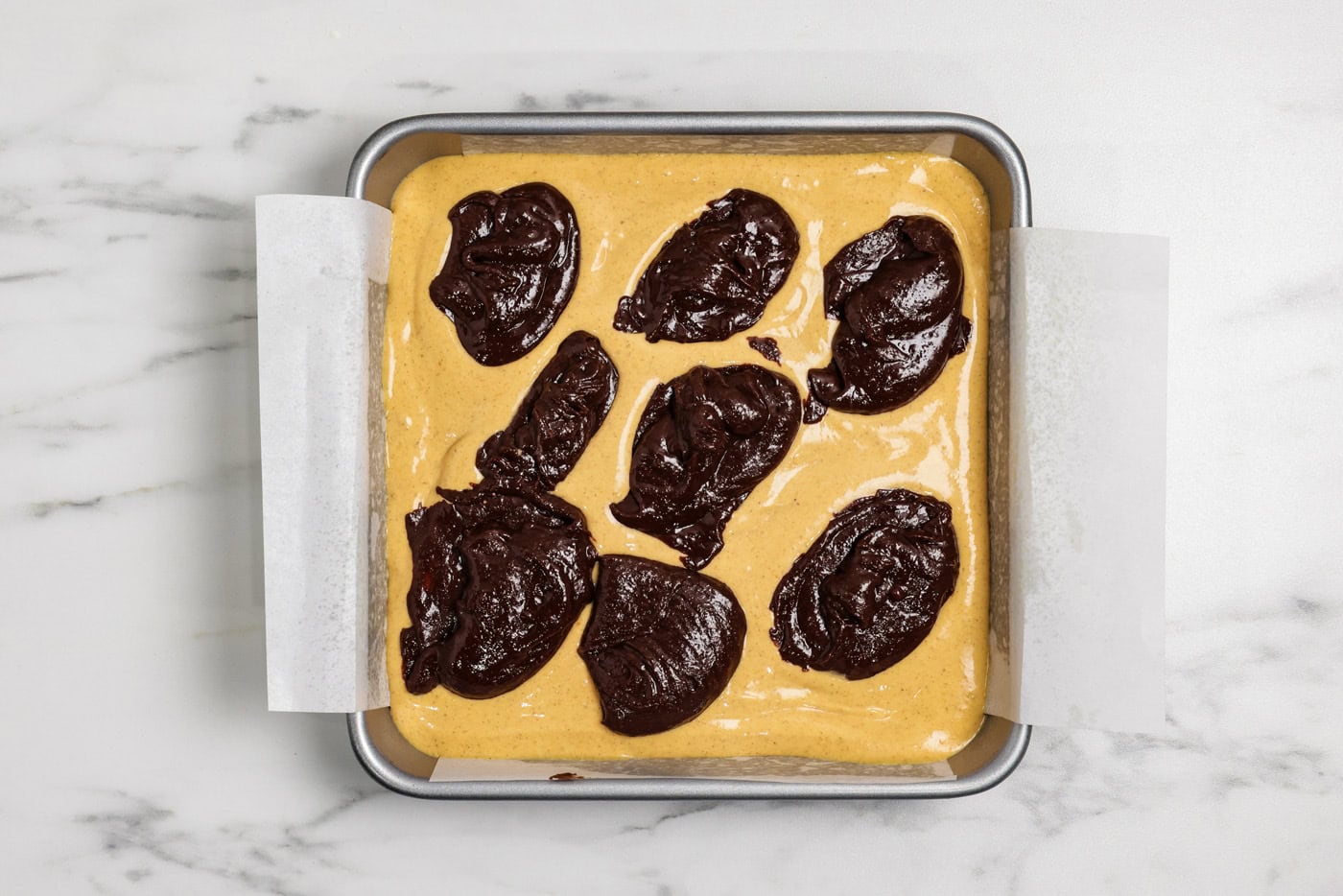 spoonfuls of brownie batter on top of pumpkin cheesecake batter layer in a pan