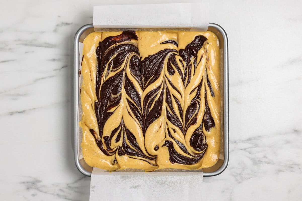swirls of brownie batter on top of pumpkin cheesecake batter in a pan