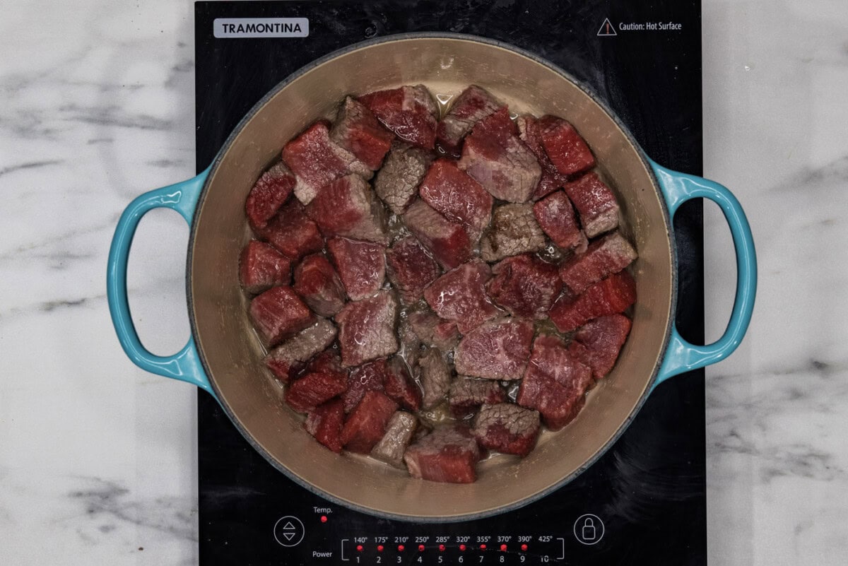 cubed beef short ribs searing in a dutch oven