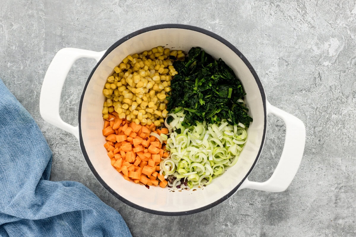 spinach, corn, carrots, and leeks added to a soup pot