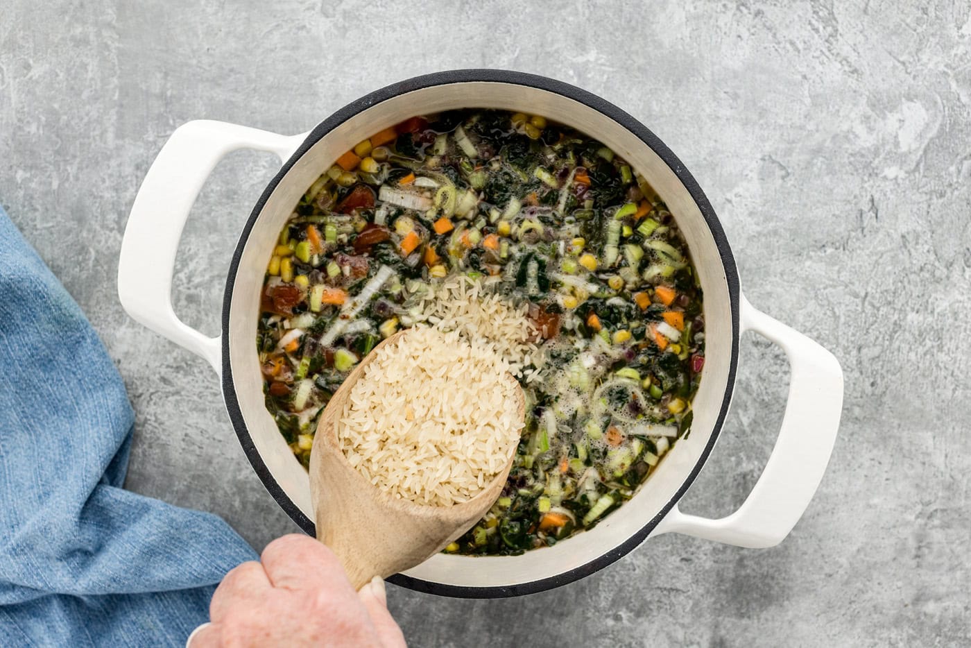 adding uncooked rice to vegetable soup in a pot