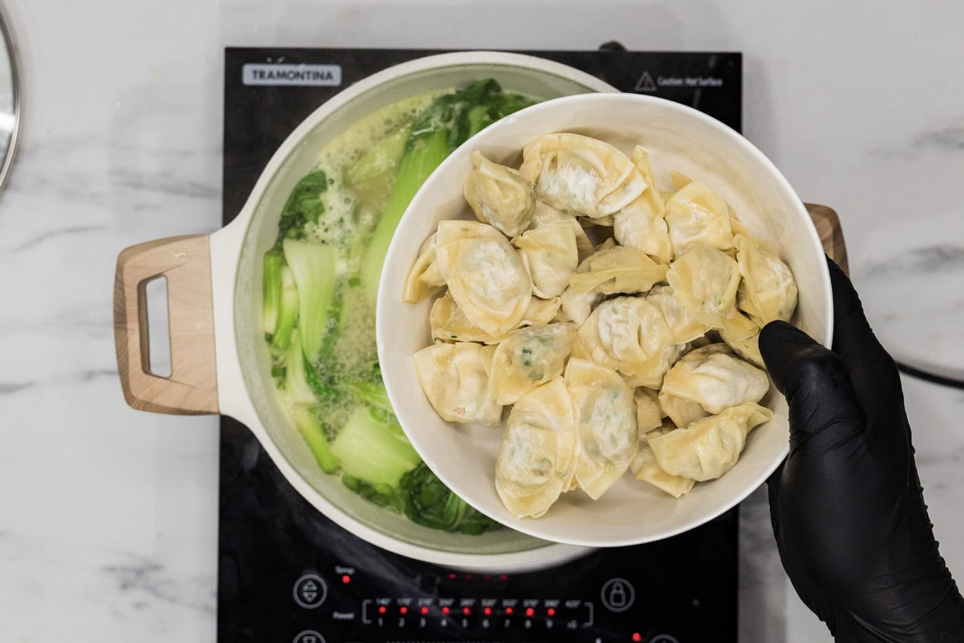 adding frozen wontons to stockpot with baby bok choy and chicken broth mixture