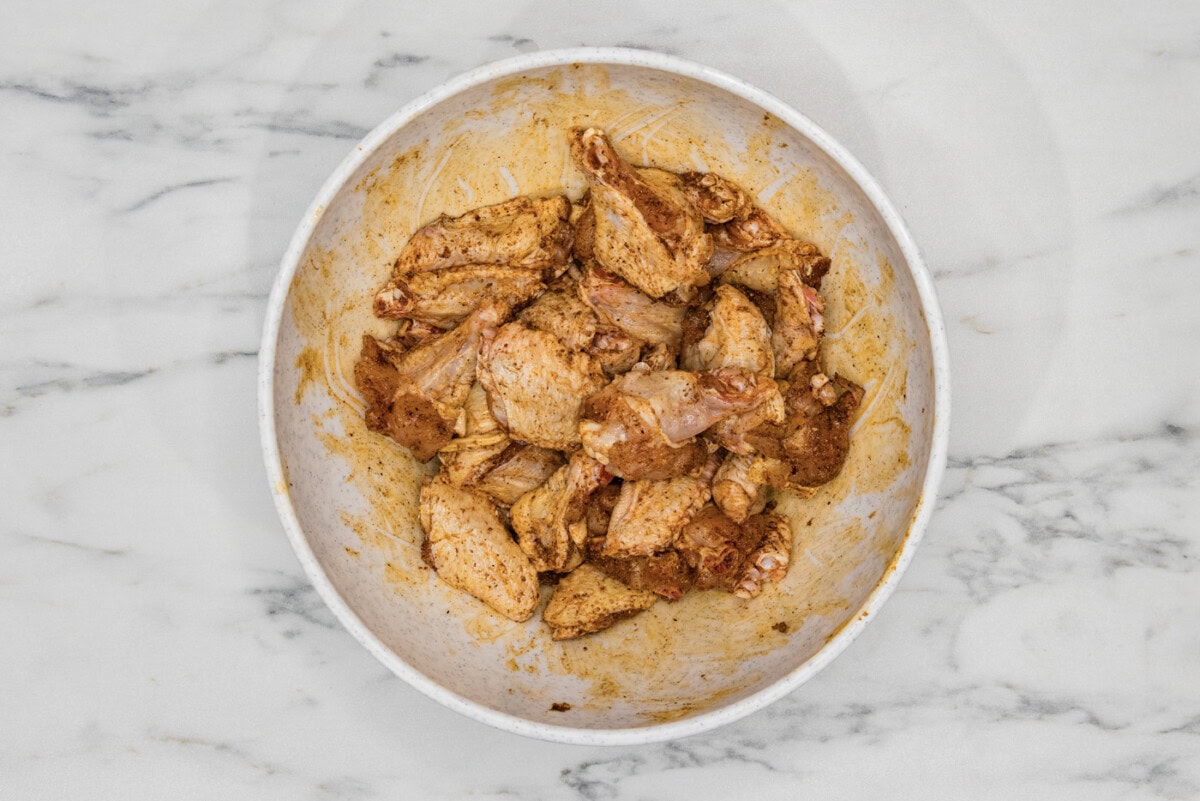 chicken wings in a bowl tossed in a rub