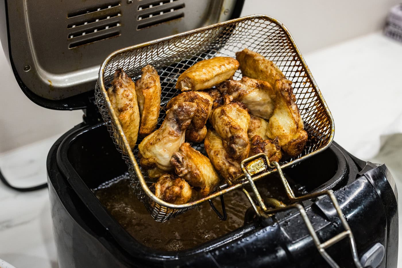 removing basket of chicken wings from a deep fryer